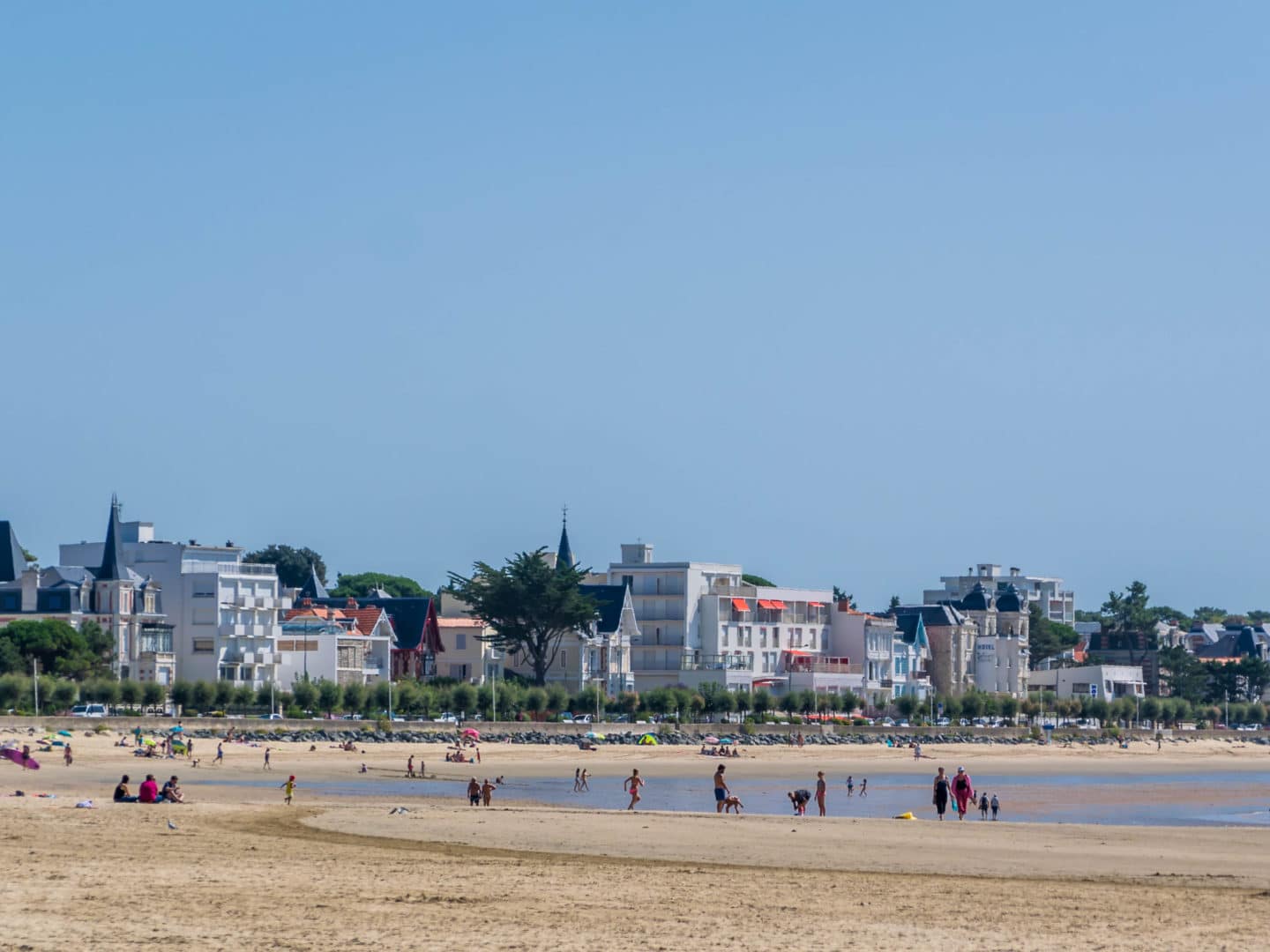 Plage de sable avec baigneurs et bâtiments en arrière-plan.