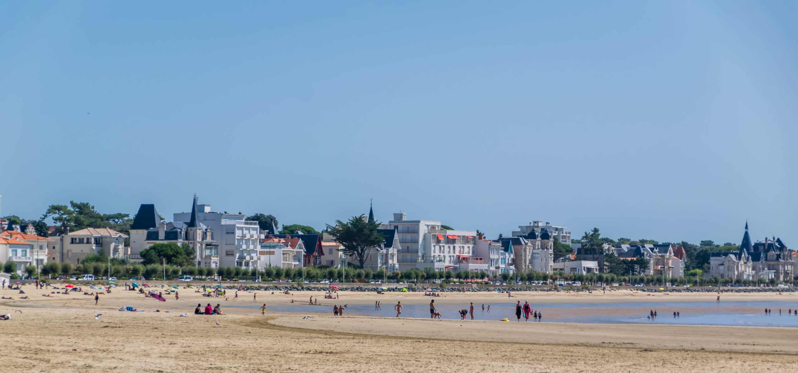 Plage de sable avec baigneurs et bâtiments en arrière-plan.