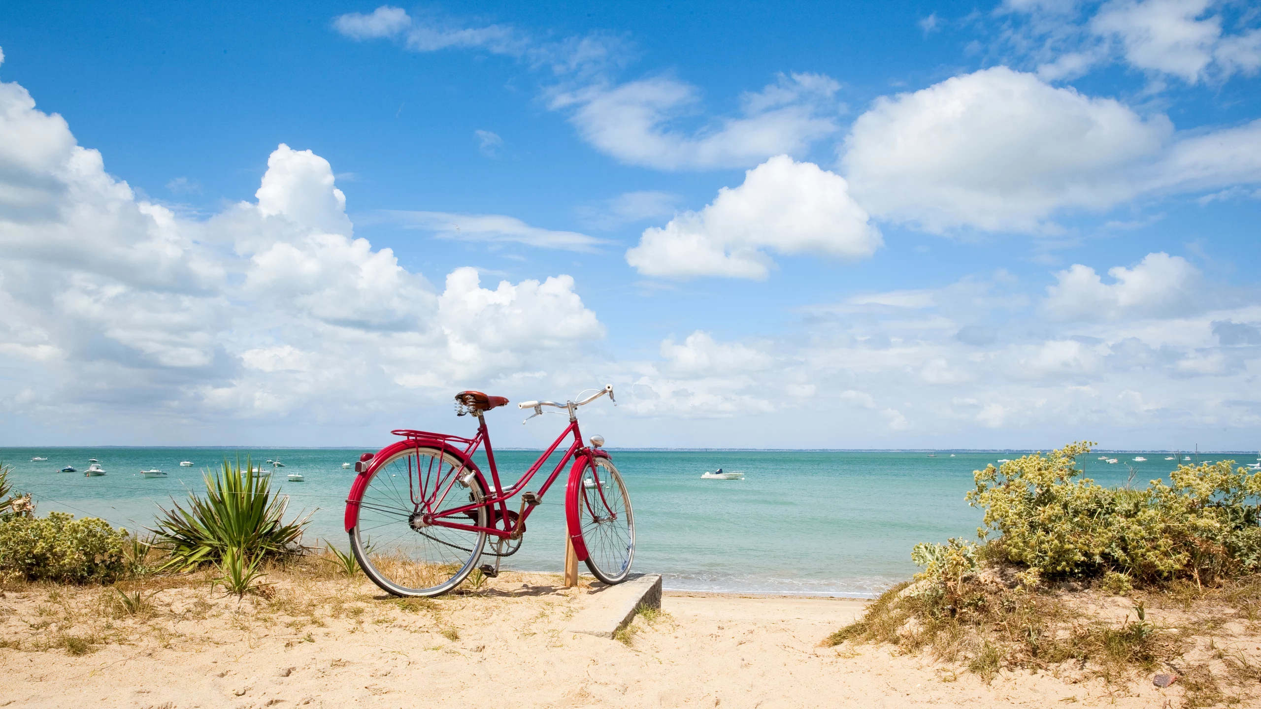 Vélo rouge sur plage sableuse, ciel bleu nuageux.