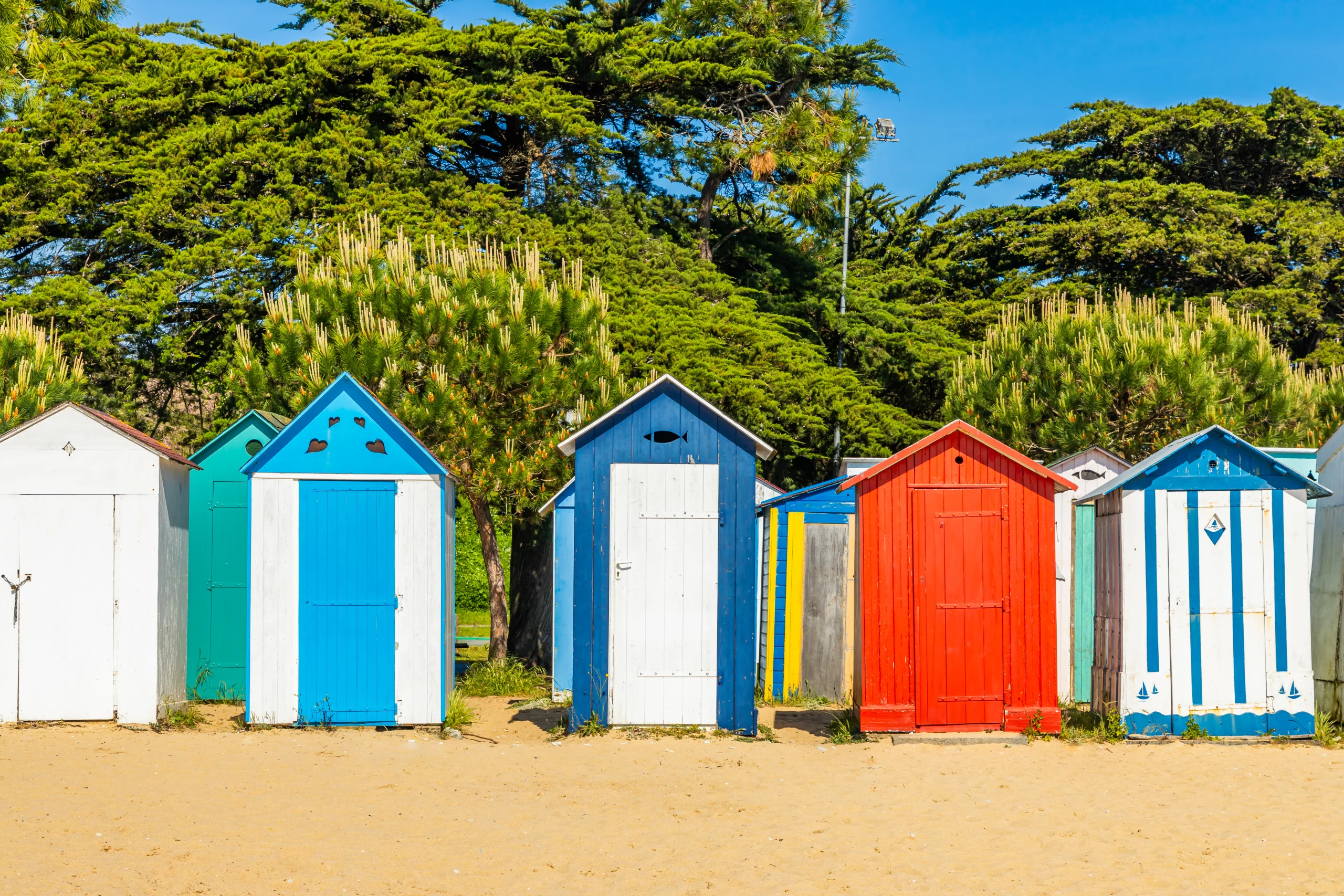 Cabines de plage colorées sur sable ensoleillé.