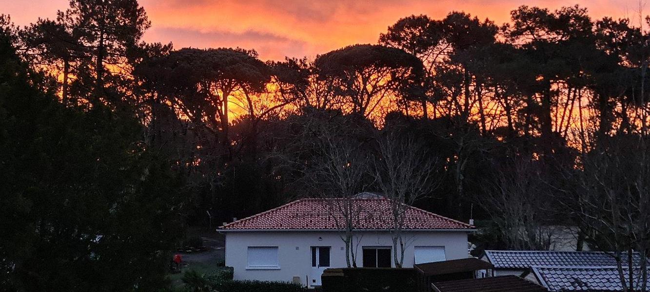 Maison au coucher de soleil derrière des arbres.