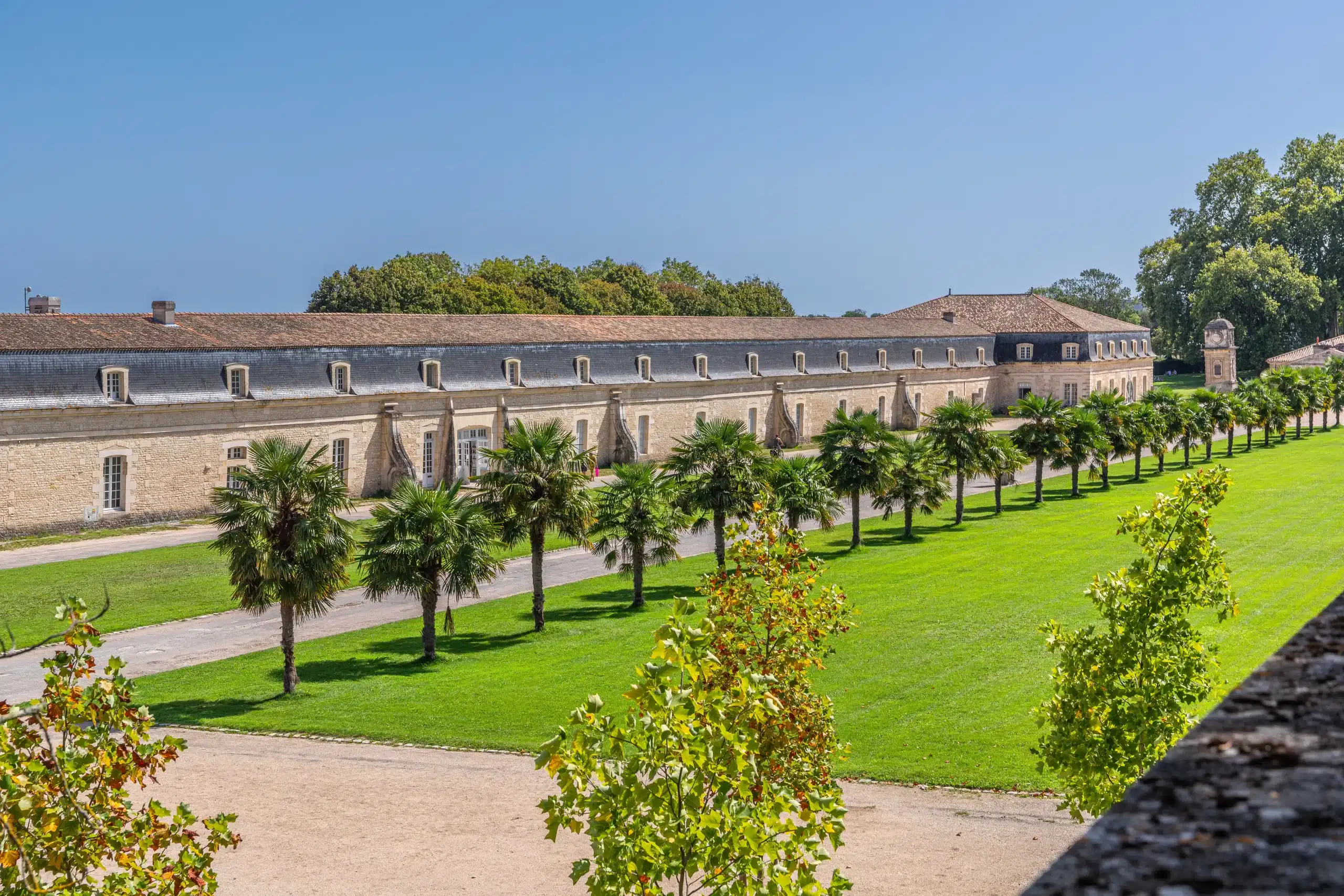 Piste cyclable bordée d'arbres et vieux bâtiment en pierres.