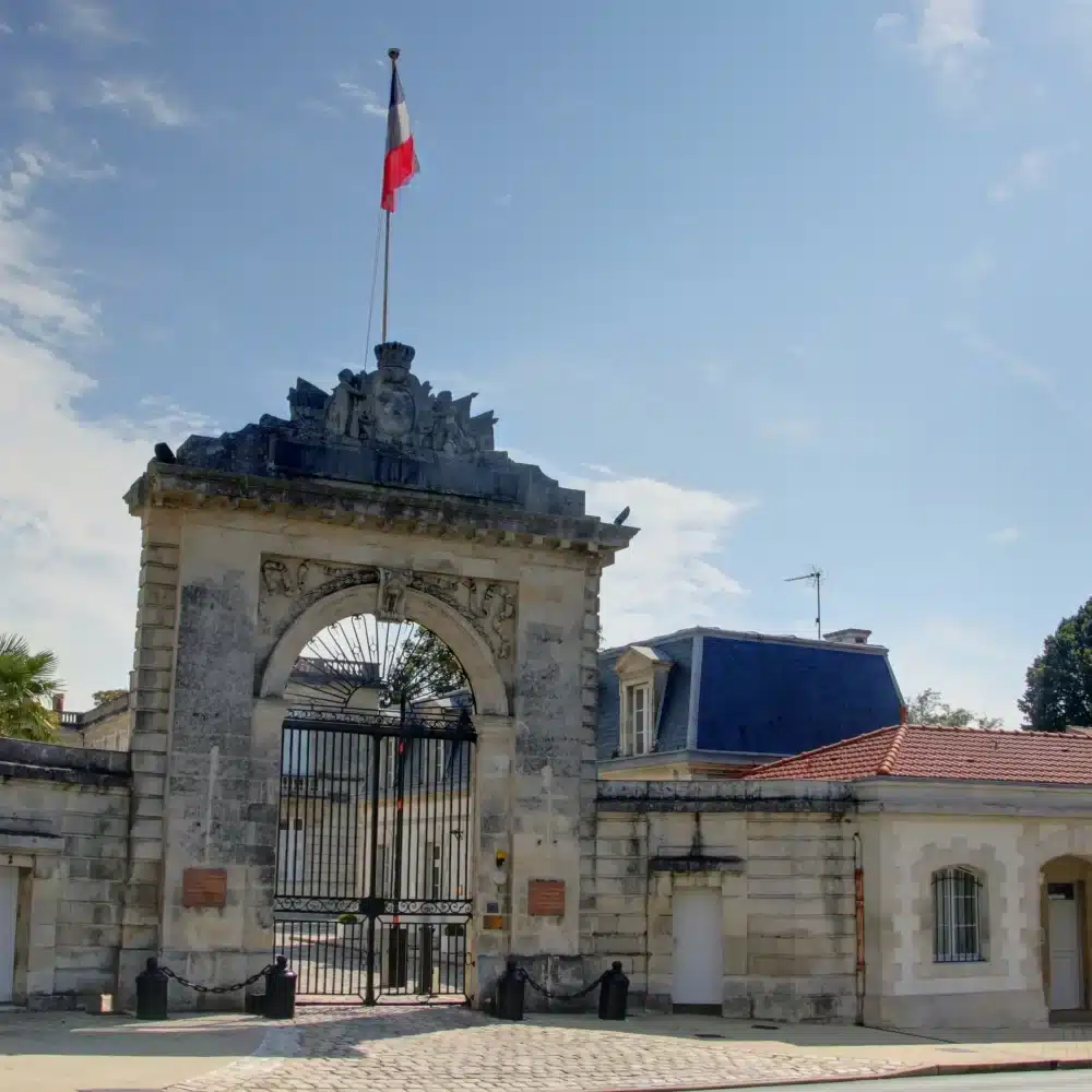 Entrée principale avec drapeau français, ciel bleu.