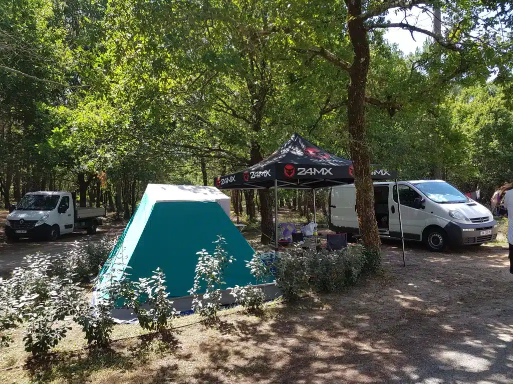 Camping avec tente et camionnettes sous les arbres.