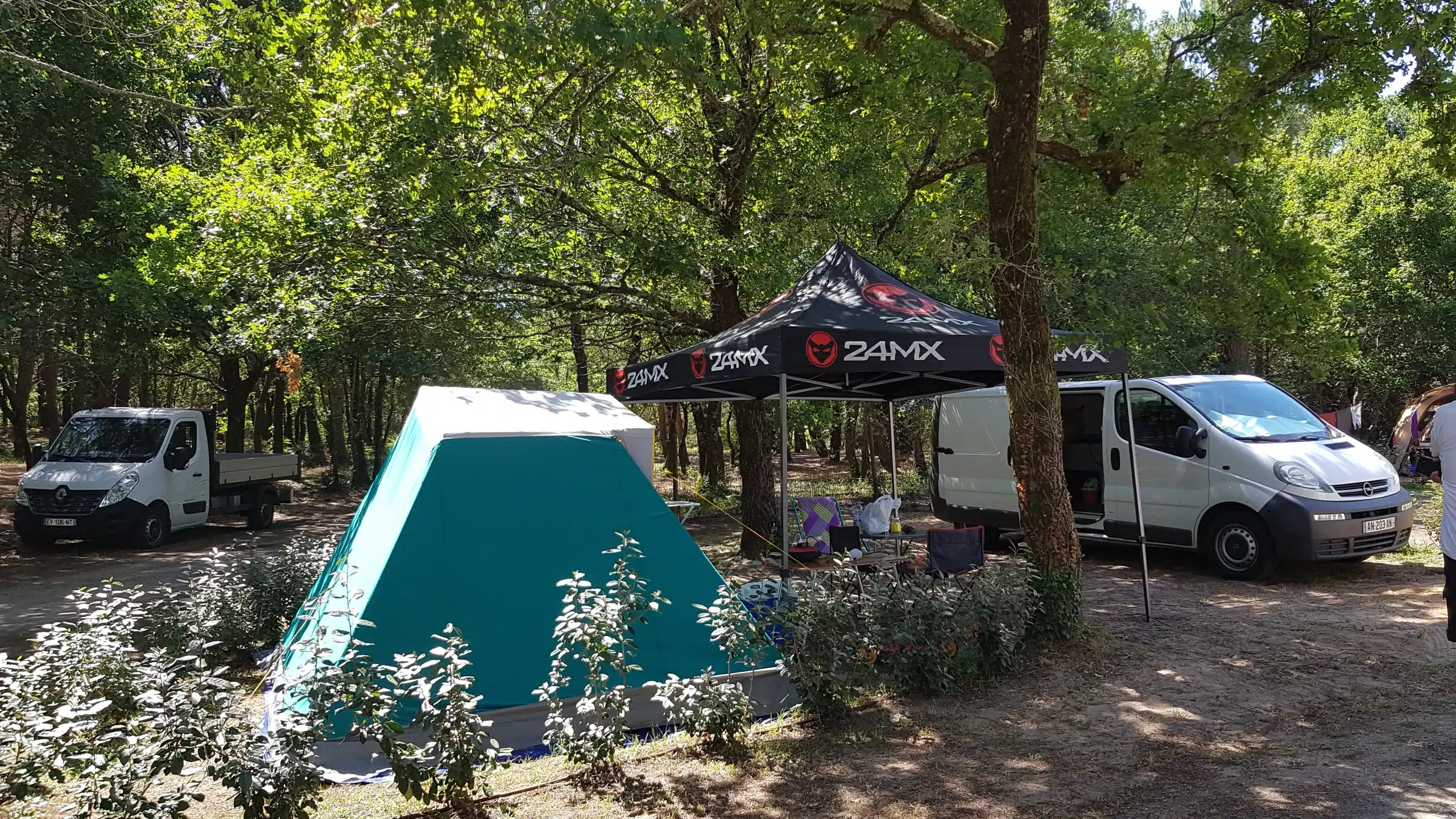 Camping avec tente et camionnettes sous les arbres.