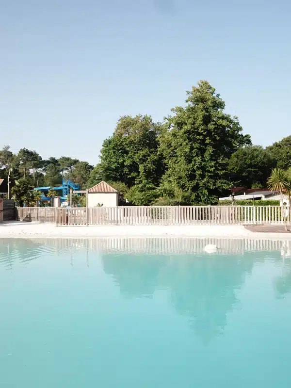 Piscine extérieure avec cabines et arbres verdoyants.
