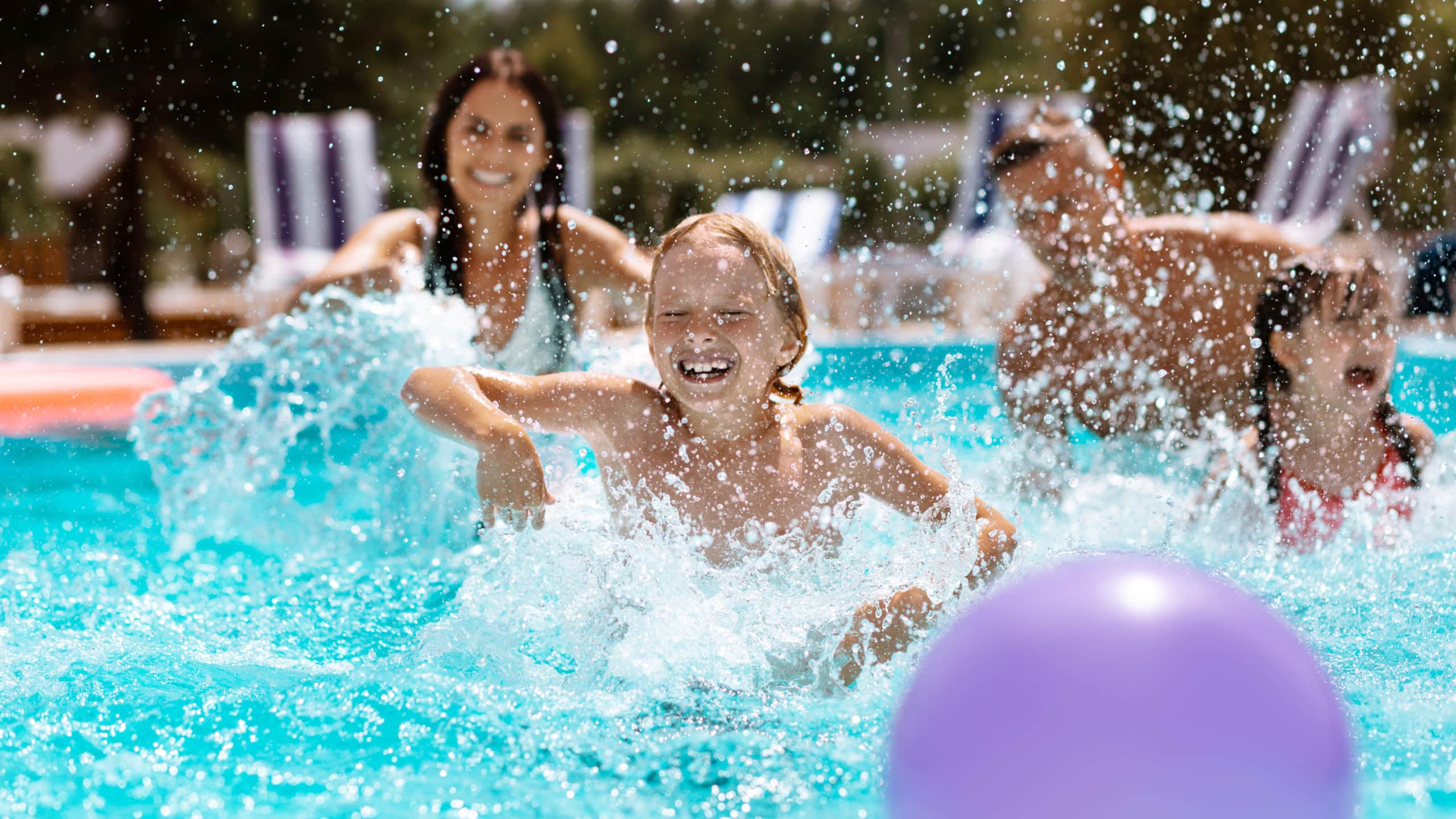 Enfants jouant dans une piscine avec ballon violet.
