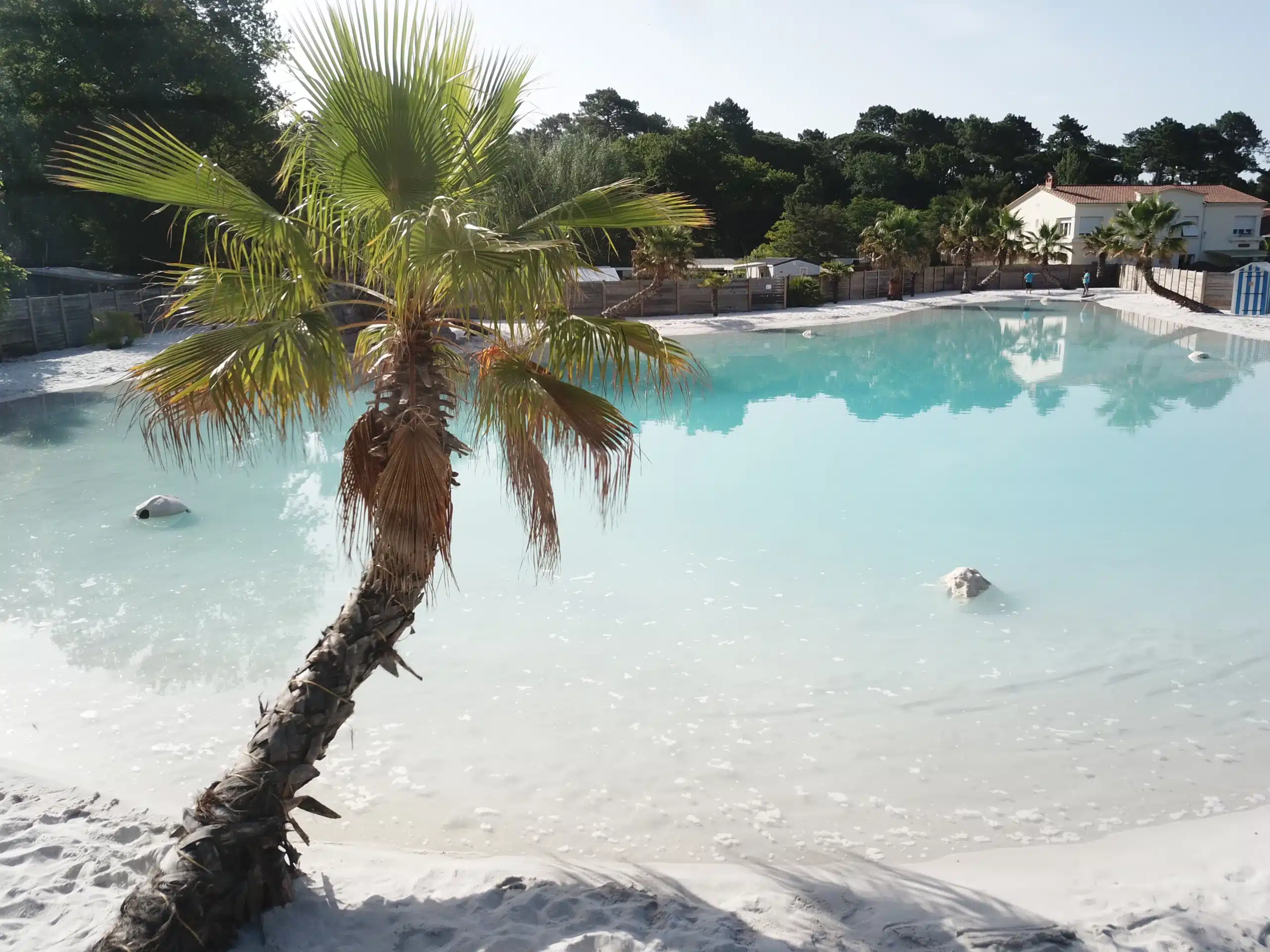 Weißer Sandstrand mit Palmen und Swimmingpool.