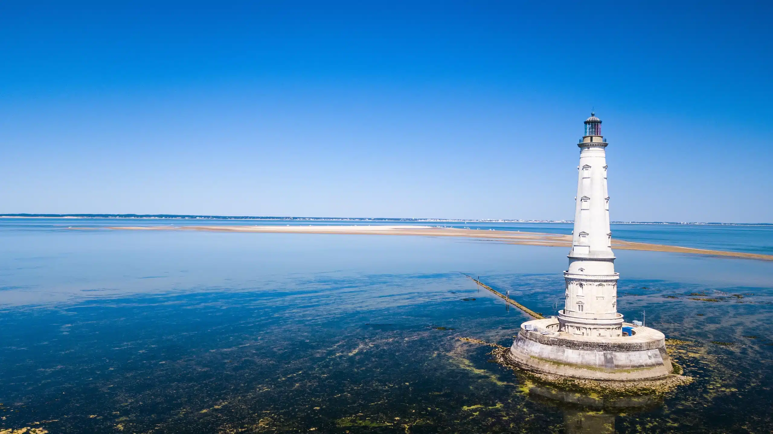 Phare blanc sur mer bleue, ciel dégagé