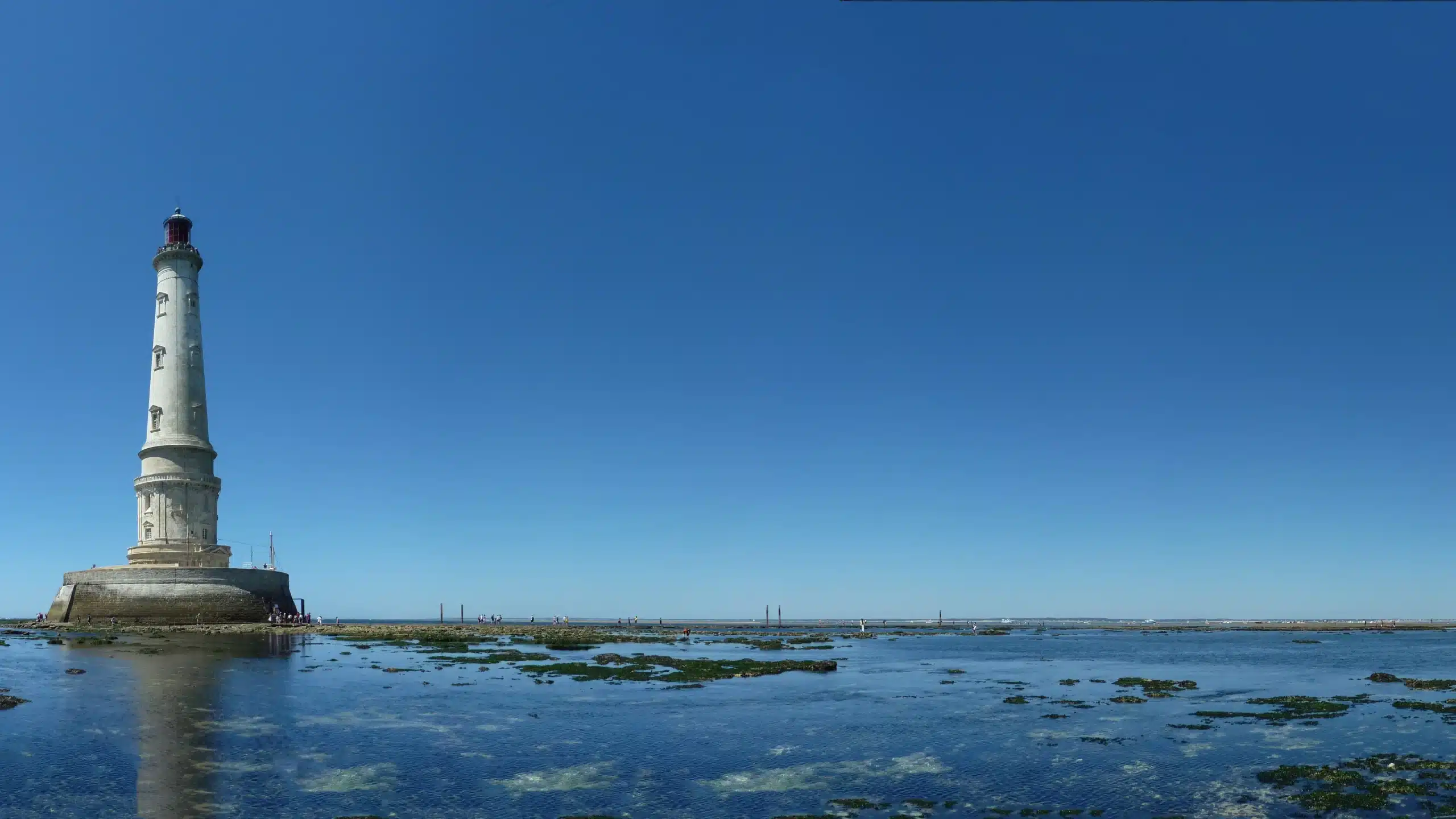 Phare sur mer à marée basse, ciel bleu.