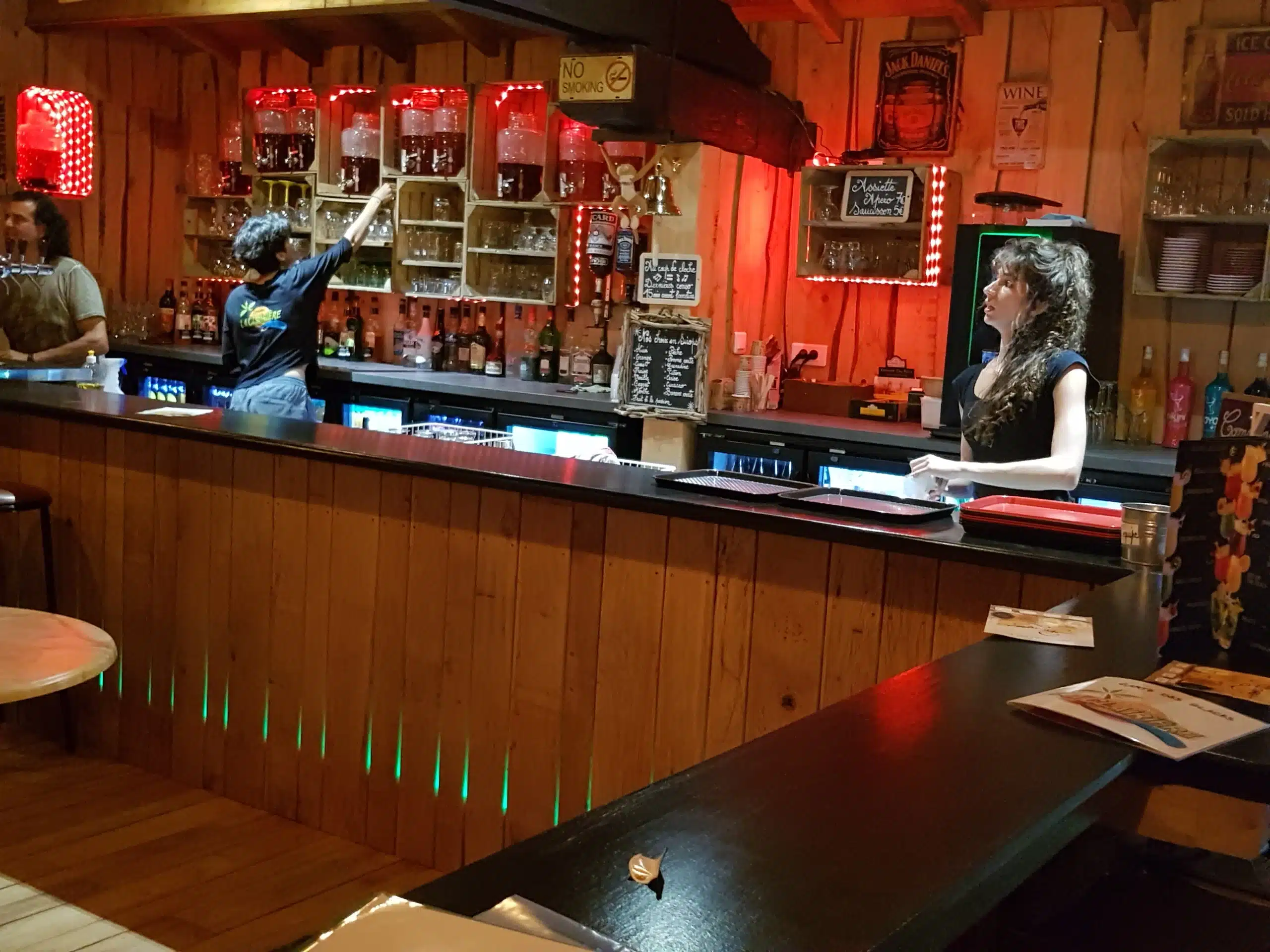 Bar avec serveurs et étagères de boissons illuminées.