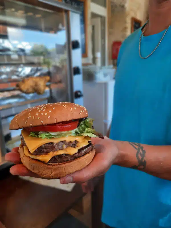 Person, die einen Hamburger mit doppeltem Käse und Gemüse hält.